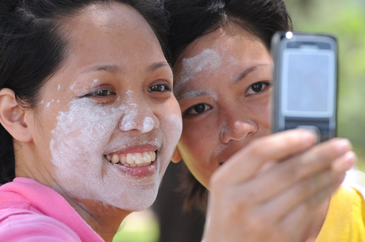 Two women take a selfie, faces with white substance.